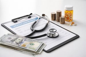 Realistic and minimalist composition showing a health insurance document on a clipboard with a stethoscope resting on top, stacks of coins, a prescription pill bottle, and US dollar bills arranged on a clean white background, illustrating the relationship between healthcare and long-term finances in the United States.